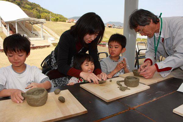 大人たちに教えてもらいながら粘土を使って土器作りをしている子供たちの写真