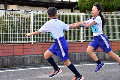 青いゼッケンのチームの女の子から男の子へタスキをつないでいる写真