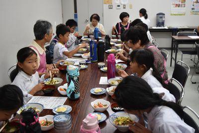 子供達と大人が一緒に座り食事をしている写真