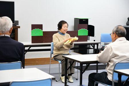 斉藤さんが手に人形を持って座っている写真