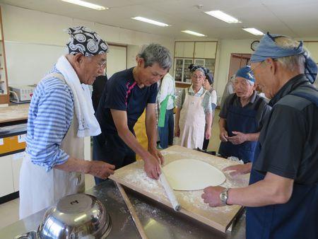 男性が棒を持ってうどんの生地を伸ばしている写真