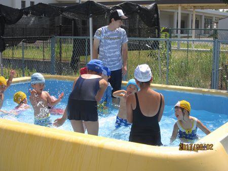 プールの中で水をかけあって遊んでいる園児と小学生の写真