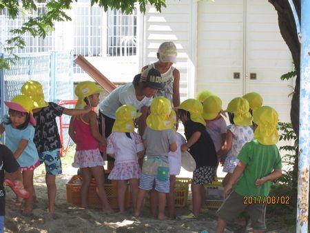 砂場遊び用の道具を園児たちに手渡している小学生の女の子と黄色い帽子をかぶった園児たちの写真