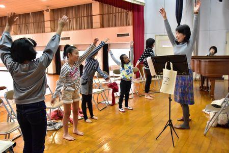 先生と生徒達が立って両手を伸ばし体を伸ばしている写真