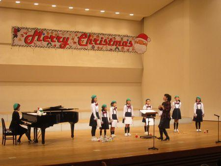 メリークリスマスと大きく書かれたボードがあるステージ上に並んでいる子供たちの写真