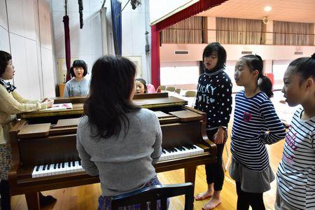 先生のピアノに合わせて発声練習をしている女の子5人の写真