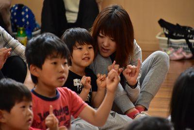 座っている保護者と子供たちが両手の小指を立てている写真