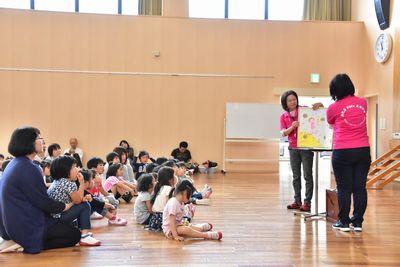 床に座っている保護者と子供たちが、スタッフが読んでいる大きな絵本をじっと見ている写真