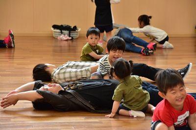 仰向けになって寝ている保護者の横に座っている子供たちの写真