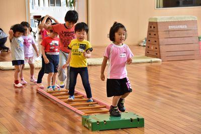 順番に並んで床の上に置かれたはしごの上を歩いている子供たちの写真