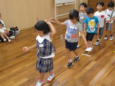 床に置かれたロープの上を子供たちが順番に並んでバランスを取りながら歩いている写真