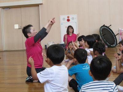 スタッフの前に座って集まっている子供たちが、スタッフの方と同じ手の動きをしている写真