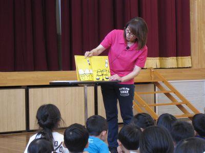 女性スタッフが横に置かれた台に絵本を置いて絵本を読んでいる写真