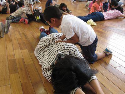 床にうつ伏せになっているお母さんの背中を触っている男の子の写真