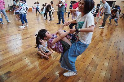 お母さんと女の子が向かい合って両手を握り、女の子がお母さんの脚を上って逆上がりをしようとしており、お母さんが重たそうに顔を歪めている写真