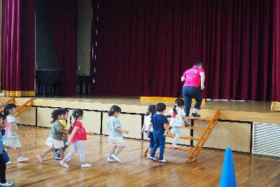 舞台に上がる階段の上をスタッフの女性が上がっており、その後ろに子ども達が一列に並んで階段を上がろうとしている写真