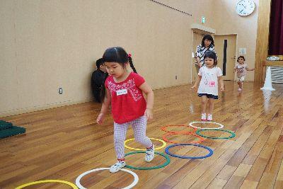 床に沢山の色の付いた輪っかが置かれケンケンパの遊びを赤いティーシャツを着た女の子がしている写真