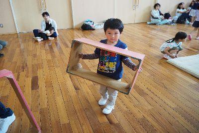 青いティーシャツを着た男の子が跳び箱の一つの木枠を両手で持って、片づけをしている写真
