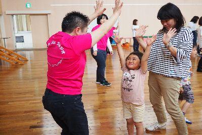 短髪のスタッフの女性が両手を上に挙げており、向かい合って立っている女の子が両手を上に挙げて、ハイタッチをしようとしている写真