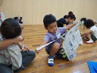 男の子が、新聞紙を細く破っている写真
