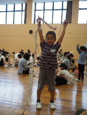 細長く破った新聞紙を高く上げている男の子の写真