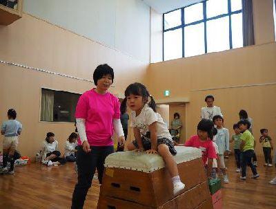 跳び箱の上をまたいでいる女の子と、その横で声をかける女性スタッフの写真