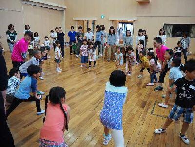 前に出した片足に両手を添えた体勢の子供たちや女性スタッフが輪になっている写真