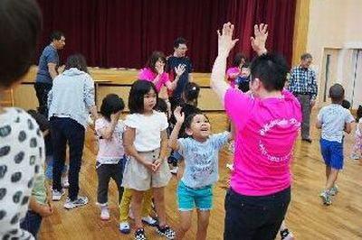 両手を上にあげている女性スタッフとハイタッチをする女の子と、その後ろに並ぶ子供たちの写真