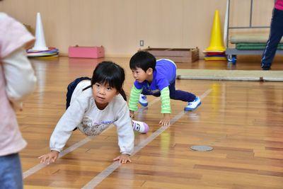 床に白い線が2本引かれていて、その上を子どもが四つん這いになって進んでいる写真