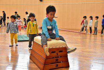 水色の服を着た男の子が跳び箱の上で足を広げて座っている写真
