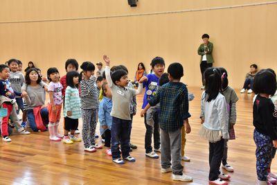 子どもたちが縦2列に並んで立っていて、中央にいる男の子が手を挙げている写真