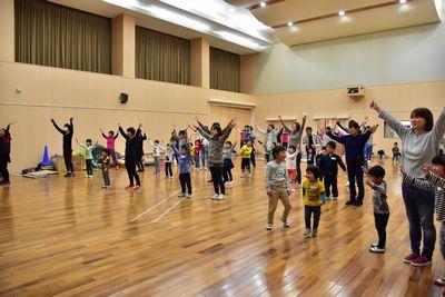 大人や子供の参加者達が両手をあげダンスをしている写真