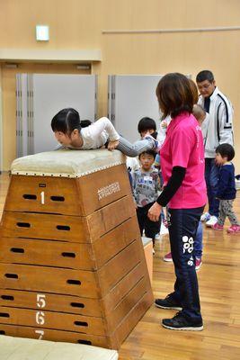 7段の跳び箱の上にお腹を付けて跳び箱を跳ぼうとしている女の子と横で見守っているスタッフの女性の写真