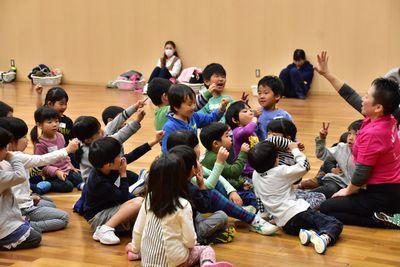 スタッフの方の周りに集まり床に座っている子供たちが片手を挙げスタッフの方とじゃんけんをしている写真