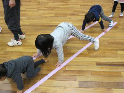 床に貼られた2本のテープの上を四つ這いで進んでいる子供たちの写真