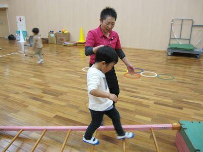 斜めに置かれたはしごの上を指導者と手を繋いで渡っている男の子の写真
