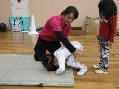 マットの上で指導者に支えられながら前回りをしている女の子の写真