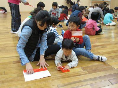 あ母さんと一緒に赤い折り紙を折っている子供たちの写真