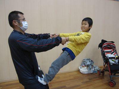 お父さんと手をつなぎお父さんの腰に足を延ばしている男の子の写真