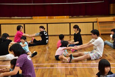 床に向き合って足を広げて座り、互いの足の裏同士をくっつけて両手をつないでいる参加者の写真