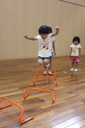 オレンジ色の小さなハードルを両足で飛び越えている女の子の写真