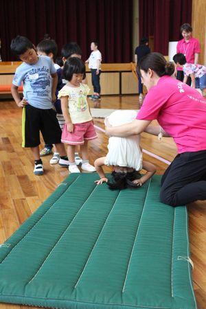 マットの上で前転をしている女の子の体を横で支えている女性スタッフの写真