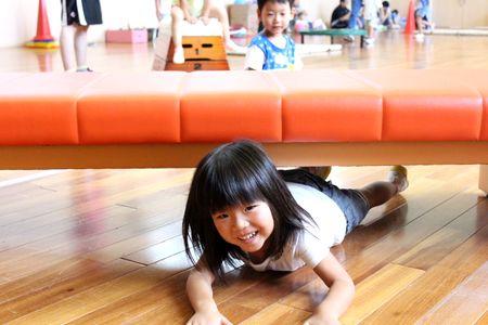 長椅子の下を腹ばいになって潜り抜けている女の子の写真