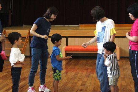 二組の親子が向かい合って立ち、青いTシャツの男の子と白いTシャツの母親がじゃんけんをしている写真