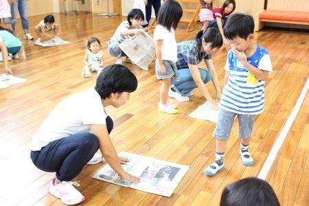 新聞紙を床に置いている母親と横に立っている男の子の写真