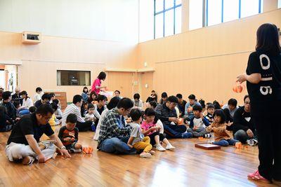 床の上で参加者の親子たちが画用紙でキャンディバックを作っている写真