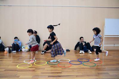 丸い輪っかが床の上に置いてあり、ケンケンパをしながら子供たちがジャンプしている写真