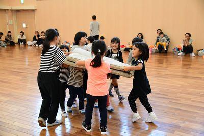 6人ほどの子どもたちが一枚の体育マットを全員で持って運んでいる写真