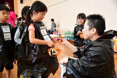 黒いビニール袋で作った仮装の衣装を着た女の子がスタッフからお菓子をもらっている写真