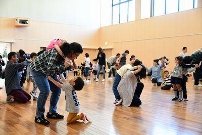 お父さんやお母さんたちが子供たちをおんぶしたりしながら体操をしている写真